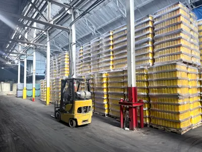 A forklift parked beside stacked pallets of yellow containers